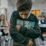 Liūdnas moksleivis su kuprine sėdi namuose ir galvoja apie mokyklą